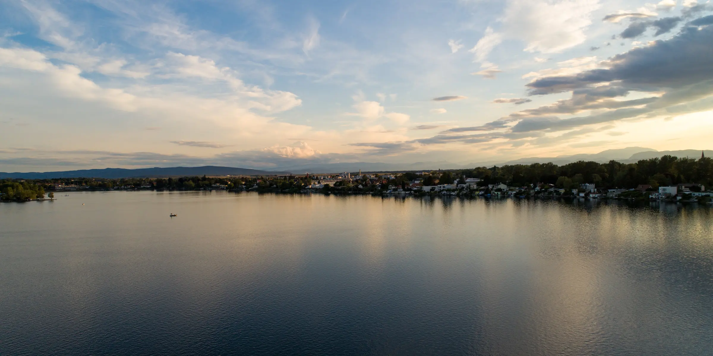 Panorama eines Sees mit Ortschaft am Ufer im Abendlicht
