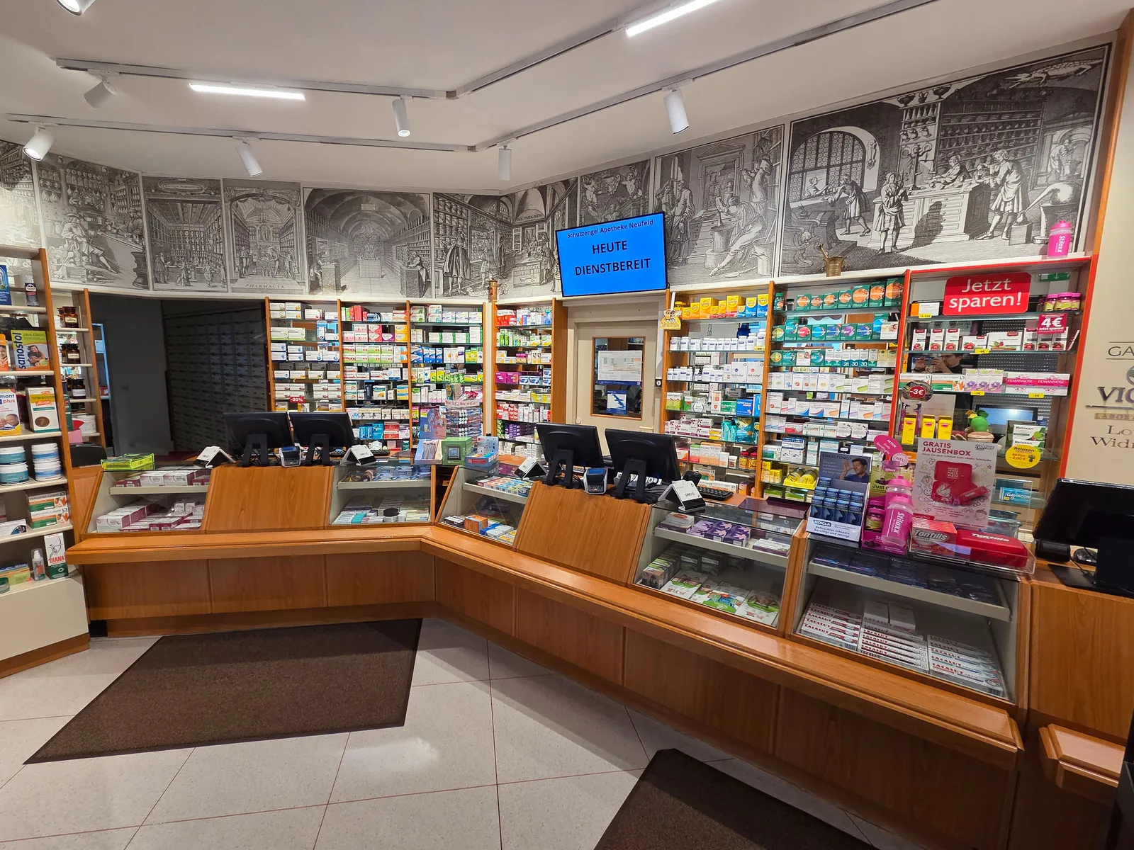 Verkaufsraum der Schutzengel Apotheke mit Holztheke, Regalen und historischen Apotheken-Wandbildern